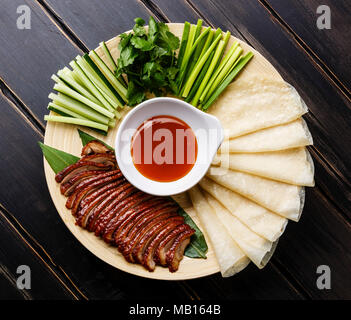 Le canard de Pékin tranché servi avec du concombre, les oignons verts, la coriandre et le froment rôti sauce Hoysin chinois avec des crêpes sur un parquet en bois noir backgroun Banque D'Images