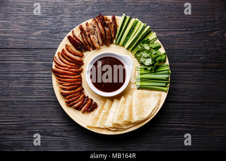 Le canard de Pékin tranché servi avec du concombre, les oignons verts, la coriandre et le froment rôti sauce Hoysin chinois avec des crêpes sur un parquet en bois noir backgroun Banque D'Images