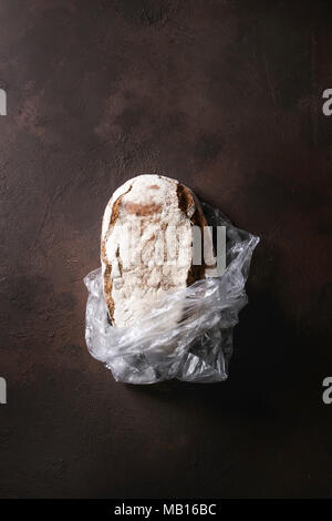 Miche de pain de seigle artisan frais cuit dans un sac en plastique brun foncé sur fond de texture. Vue de dessus, copiez l'espace. Banque D'Images