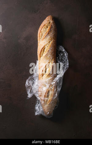 Miche de pain baguette artisan frais cuit dans un sac en plastique brun foncé sur fond de texture. Vue de dessus, copiez l'espace. Banque D'Images