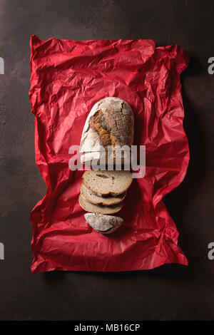 Tranches de pain frais cuit de pain de seigle artisan sur papier froissé rouge brun foncé sur fond de texture. Vue de dessus, copiez l'espace. Banque D'Images