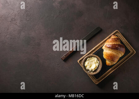 Des petits croissants traditionnels en bois sur l'ardoise avec du beurre et du conseil vintage couteau sur dark brown texture background. Vue de dessus, copy space Banque D'Images