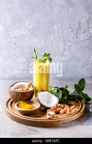 Tasse de lait de coco d'or Verre ayurvédique curcuma poudre de curcuma avec latte glacé, glace pilée, menthe et ingrédients ci-dessus sur plateau de bois rond sur Banque D'Images