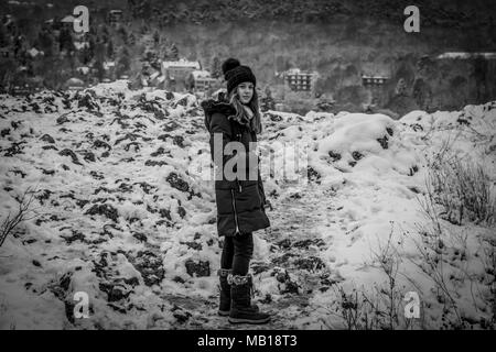 Jolie teen girl in snow, face caméra, noir et blanc. Belle Caucasian teenage girl in manteau noir, les montagnes enneigées en arrière-plan. Banque D'Images