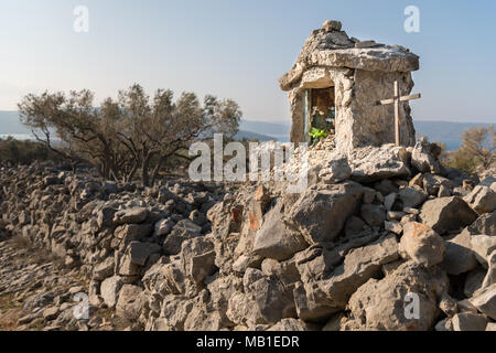 Petite chapelle blanche et une croix de métal sur un mur de pierre près de Cres Croatie lors d'une journée ensoleillée au printemps Banque D'Images