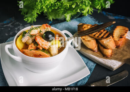 Soupe de poisson française Bouillabaisse aux fruits de mer, filet de saumon, crevettes, saveur riche, délicieux dîner dans un beau plat blanc. Close up. Banque D'Images