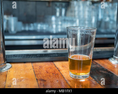 Presque vide pint verre de bière assis sur woodencountertop pour le dernier appel. Bar en arrière-plan Banque D'Images