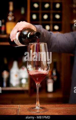 Dans un verre de vin rouge le barman verse une bouteille de vin Banque D'Images