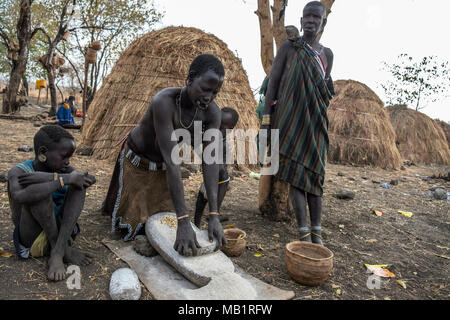 L'Éthiopie, Omorate - 24 janvier 2018 : les femmes de la tribu Mursi sont le meulage des céréales avec une pierre pour préparer la farine dans l'Éthiopie. Banque D'Images