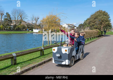 Les jeunes passagers de monter sur un véhicule motorisé de l'enfant dans un parc, tout en agitant à personnes, au Royaume-Uni. Banque D'Images