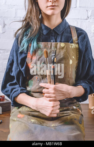 Portrait de l'artiste féminine assis sur table et holding pinceaux Banque D'Images