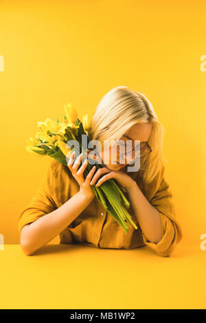 Belle Jeune femme tenant des fleurs de printemps jaune sur jaune Banque D'Images