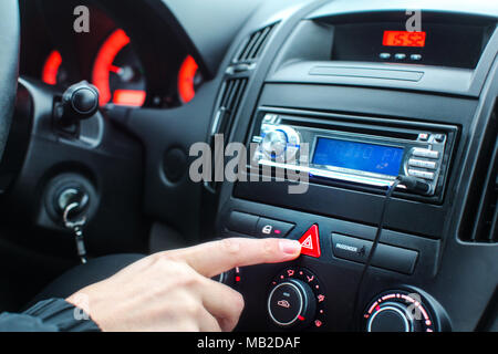 Détail sur le tableau de bord de voiture, l'homme doigt qui appuie sur le bouton d'éclairage d'urgence pendant la conduite. Banque D'Images