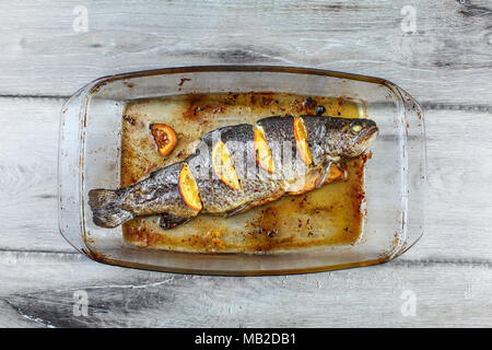 Vue de dessus de table sur la truite grillée avec des citrons dans un moule en verre, sur bois gris 24. Banque D'Images