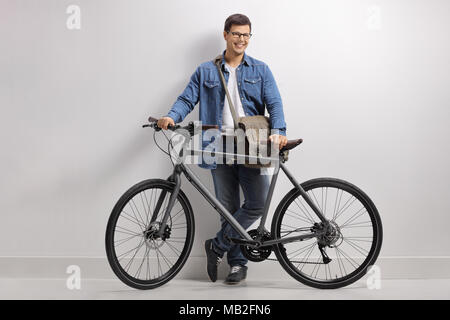 Portrait d'un jeune homme avec un vélo appuyé contre un mur et souriant Banque D'Images
