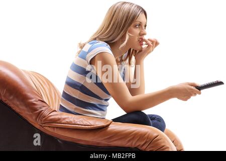 Jeune femme assise dans un fauteuil à regarder la télévision et de mordre ses ongles isolé sur fond blanc Banque D'Images