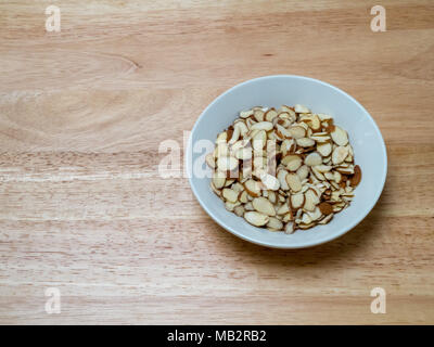 De l'angle de la porcelaine bol rempli d'amandes tranchées sur billot avec certaines espace sur la droite avec un peu d'espace d'ombre sur la gauche Banque D'Images