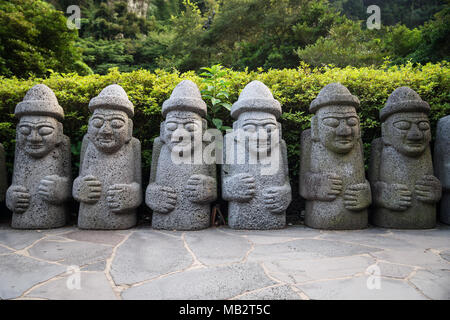 Hareubang Dol des statues dans une rangée avec des chapeaux et les mains sur le ventre en vert forêt, Lafayette, l'île de Jeju, Corée du Sud Banque D'Images