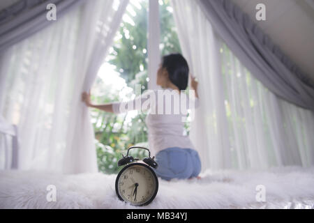 Jeune femme en ouvrant les rideaux de la fenêtre d'appartements moderne après service Banque D'Images