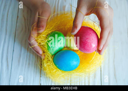 Les oeufs de Pâques colorés sur fond de bois blanc dans les mains de l'enfant. Banque D'Images