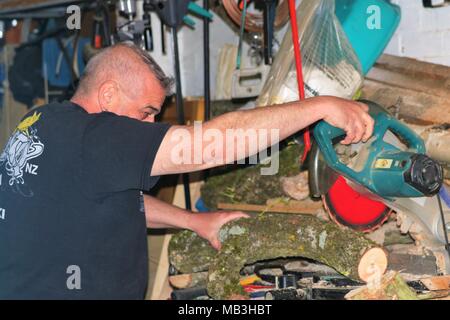 Homme d'âge moyen de couper un journal à l'aide d'une tronçonneuse / scie à onglet dans un garage encombré et ne portait aucun équipement de sécurité Banque D'Images