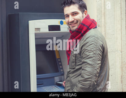 Bel homme confiant dans l'insertion d'une carte en plastique d'extérieur en ATM machine and smiling at camera. Banque D'Images