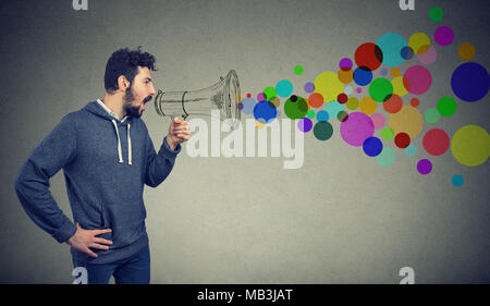 Portrait young man holding crier dans un mégaphone isolé sur fond gris. La propagande, breaking news, social media communication concept Banque D'Images