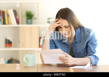 Worried woman reading de mauvaises nouvelles dans une lettre sur une table à la maison Banque D'Images