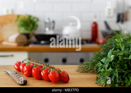 Les tomates en vigne sur vigne sur en bois à côté d'un couteau de cuisine et d'herbes fraîches. Hors focus accueil cuisine arrière-plan. Banque D'Images