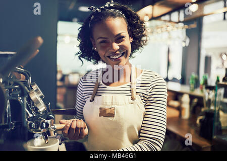 De jeunes Africains et la préparation d'un smiling barista tasse de café tout en se tenant à une machine à café dans un café branché Banque D'Images