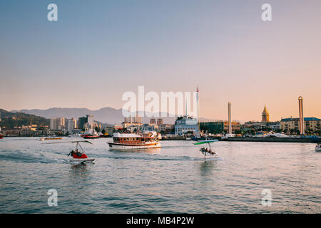 Batumi, Géorgie, l'Adjarie. Petit plaisir Bateau de tourisme pour la croisière et des deltaplanes près de la côte dans la soirée d'été. Bâtiment de la gare maritime en se Banque D'Images