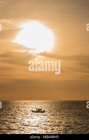 Petit bateau en mer sous un soleil orange colorés silhouette sur le reflet lumineux émis par le soleil couchant sur l'eau Banque D'Images