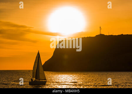 Voilier bateau à passé une silhouette pointe lors d'un casting spectaculaire coucher du soleil orange vif une réflexion sur l'océan calme Banque D'Images