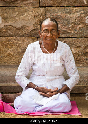 Portrait vertical d'une vieille dame en méditant à Jaya Sri Maha Bodhi dans Anuradhapura, Sri Lanka. Banque D'Images