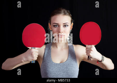 L'athlète tient dans ses mains deux chaussures de tennis de table sur un fond noir. Banque D'Images