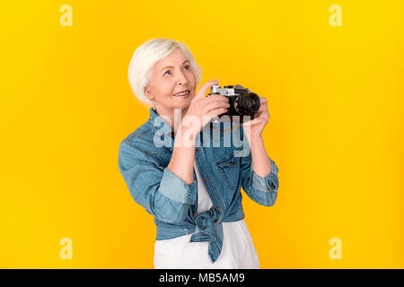 Des femmes plus âgées meilleur studio isolé sur fond jaune à prendre des photos sur l'appareil photo professionnel enthousiaste à la bonne chance Banque D'Images