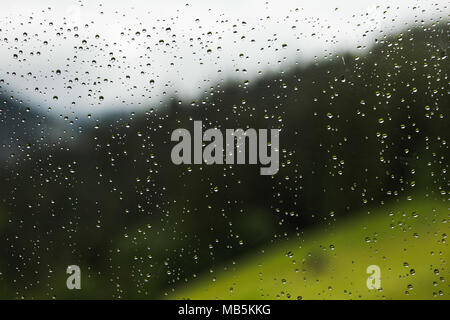 Gouttes de pluie sur la vitre de la fenêtre du chalet de campagne. À voir flou vert forêt et collines de montagne derrière le verre. Couleur horizontal pho Banque D'Images