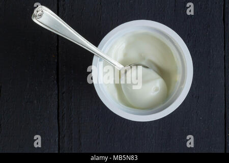 Tasse de yogourt naturel avec du yaourt grec en godet en plastique avec cuillère en argent libre sur l'arrière-plan du tableau noir rustique - Top voir photo Banque D'Images