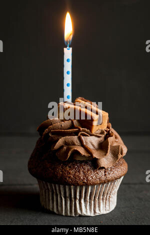 Tasse de chocolat gâteau décoré avec glaçage buttercream et fudge carrés avec bougie allumée sur fond noir Banque D'Images