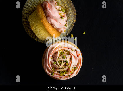 Deux gâteaux de tasse rose avec pistache saupoudre sur fond noir, vue du dessus photographie Banque D'Images