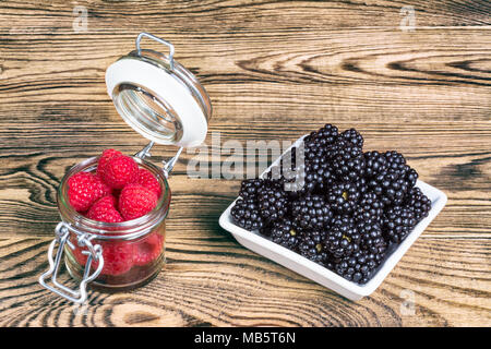 Framboises et mûres décorative sur bois magnifique arrière-plan. De délicieux fruits des bois mûrs dans un bocal en verre et bol carré blanc sur la table de jardin. Banque D'Images