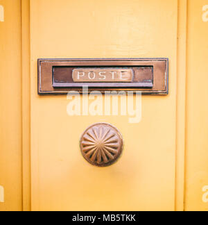 Ancienne boîte aux lettres courrier en laiton et bouton de porte sur une porte jaune, texte poste Banque D'Images