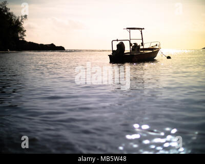Low angle d'un petit bateau à moteur ancré en silhouette lors d'un coucher de soleil aux Seychelles Banque D'Images