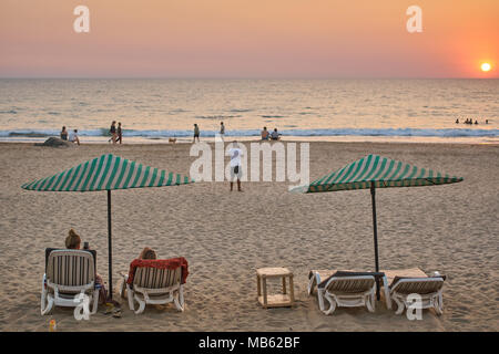 Coucher de soleil sur les touristes et les chaises longues de plage d'Agonda, Goa. Banque D'Images