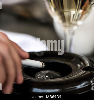 Cigarette dans un cendrier avec un verre de vin blanc Banque D'Images