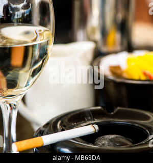 Cigarette dans un cendrier avec un verre de vin blanc Banque D'Images