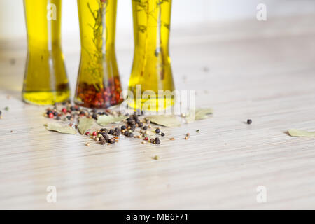 Graines de poivre colorés sur la table de cuisine et 3 bottes d'huile d'olive avec spieces, le romarin, le poivre, l'origan, le piment, la feuille de laurier en arrière-plan Banque D'Images