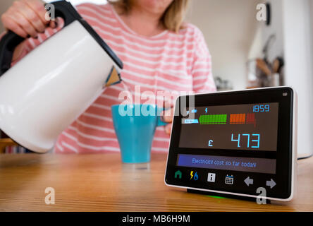Moniteur d'énergie ( compteur intelligent )dans la cuisine d'une maison comme une femme fait une tasse de thé Banque D'Images