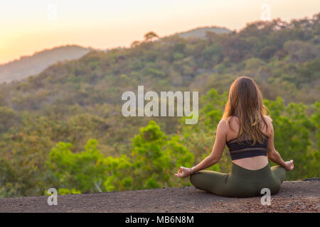 Fille assise et méditant devant un lever de soleil sur une vallée de montagne. Banque D'Images