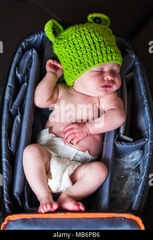 Notre fille semaine endormi dans mon sac photo portant un chapeau de grenouilles. Banque D'Images